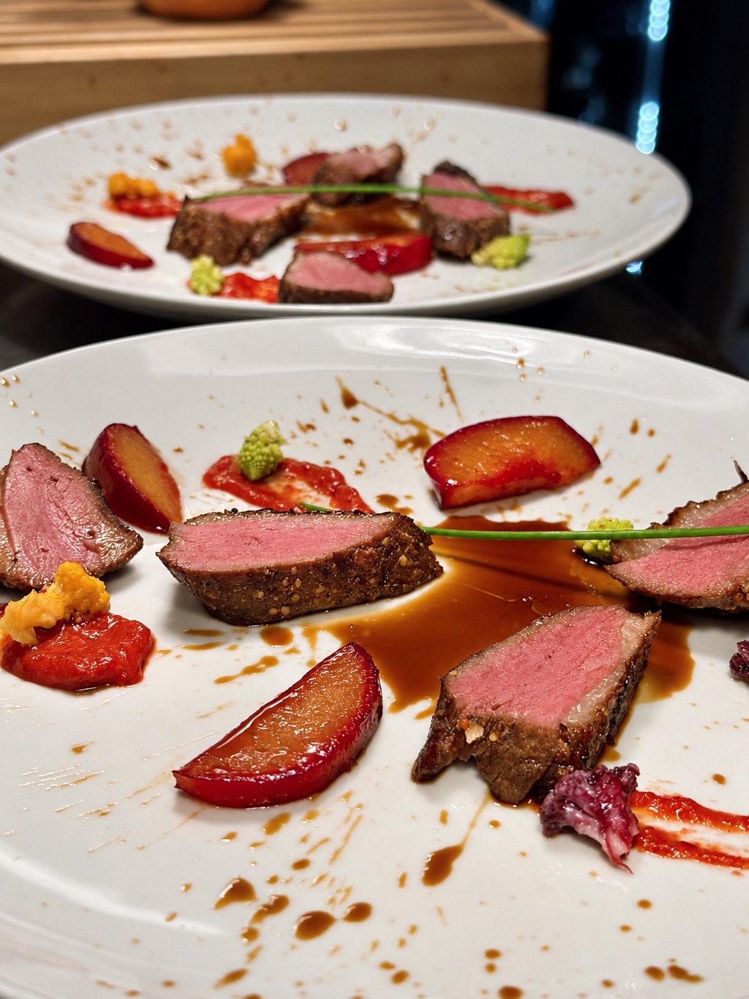 Due piatti dalla cucina di Cantina Veggiani, con carne rosata, frutta e salse su porcellana bianca